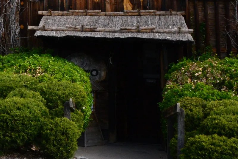 Rustic thatched-roof entry gate flanked by manicured bushes at Domo Japanese Country Foods Restaurant in Denver