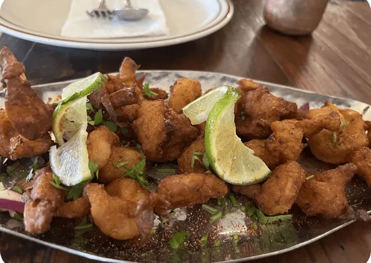Prawns koliwada — batter-fried prawns garnished with lime wedges and cilantro on a metal platter at Swaraj India, Santa Clara