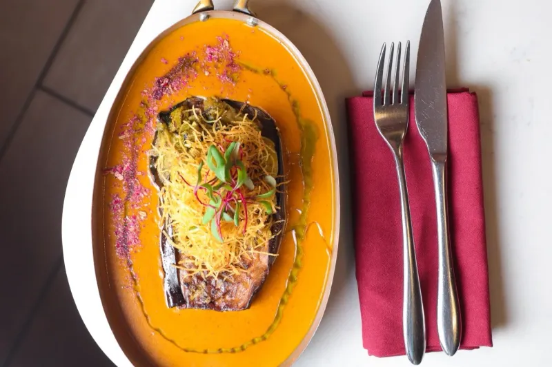 Roasted Indian eggplant plated in a copper dish with orange curry sauce at ROOH Columbus
