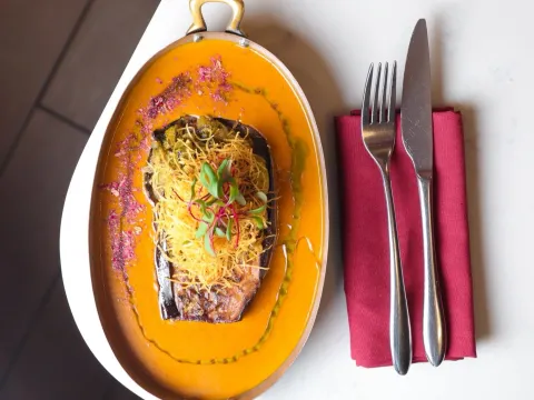 Roasted Indian eggplant plated in a copper dish with orange curry sauce at ROOH Columbus