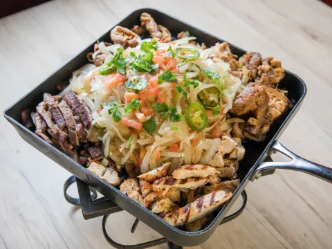 Sizzling parrillada skillet with grilled carne asada, chicken, carnitas and chicharron topped with onions, jalapenos, tomato and cilantro at Comedor Guadalajara
