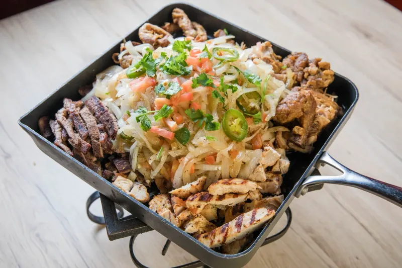 Sizzling parrillada skillet with grilled carne asada, chicken, carnitas and chicharron topped with onions, jalapenos, tomato and cilantro at Comedor Guadalajara