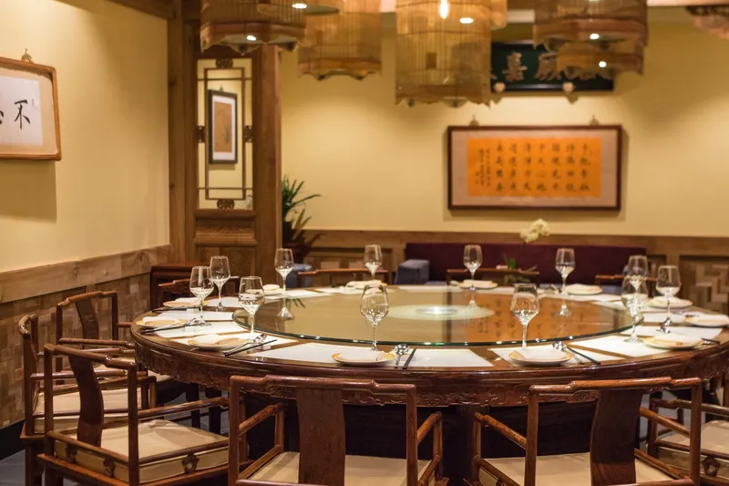 Private dining room at Bistro Na's with a round banquet table, carved redwood chairs, birdcage lanterns and framed Chinese calligraphy