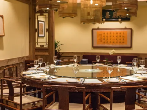 Private dining room at Bistro Na's with a round banquet table, carved redwood chairs, birdcage lanterns and framed Chinese calligraphy