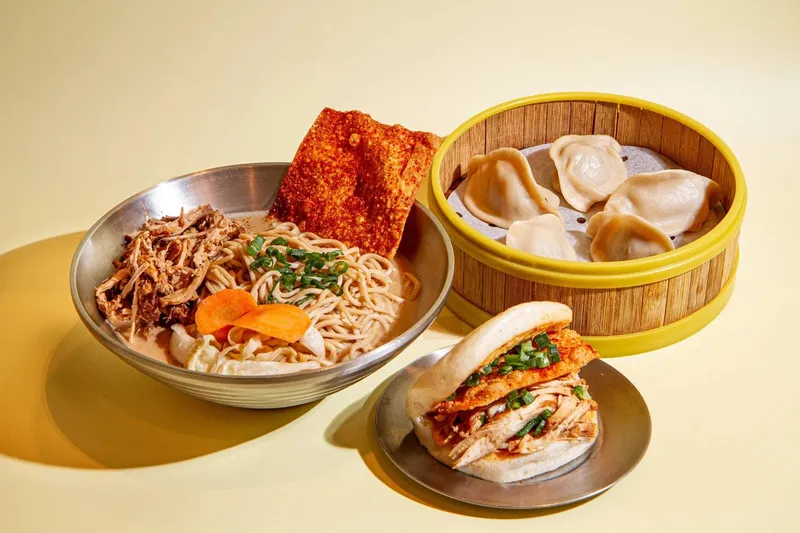 Three Fold spread in Little Rock — a bowl of braised-pork noodle soup with a crispy chili cracker, a bamboo steamer of dumplings, and a steamed bun filled with fried chicken and pulled pork