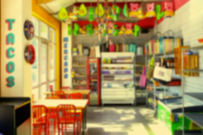 Interior of Taco Naco KC in Kansas City with a blue 'TACOS' wall sign, a 'Mercado' shelf of Mexican grocery goods, papel picado banners, and red chairs at white tables