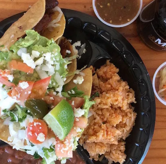 A plate of Taqueria El Bajio tacos dorados topped with guacamole, queso, tomato and jalapeño, served with Mexican rice and salsa
