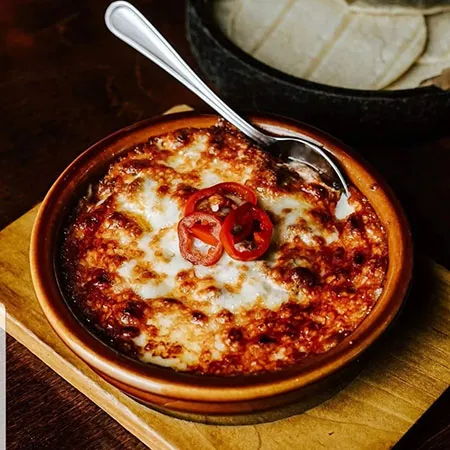 Baked queso fundido with sliced peppers at Momocho